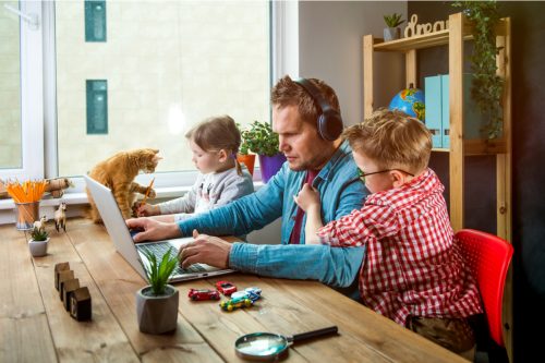 man working at kitchen table while kids and cats bother him
