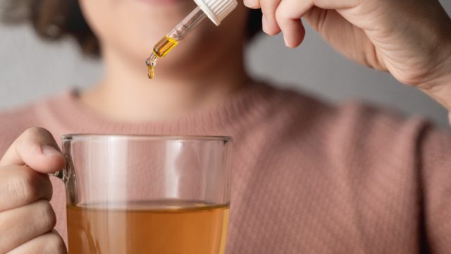 Cbd hemp oil - Woman taking cannabis oil in tea cup - Focus on drop