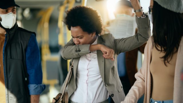 businesswoman coughing into elbow while traveling by public transport.