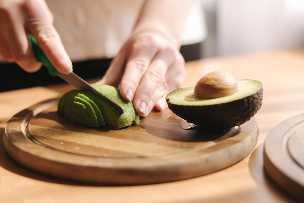 Closeup of a person slicing an avocado on a cutting board