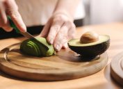 Closeup of a person slicing an avocado on a cutting board