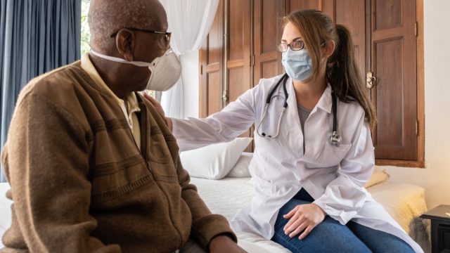 Doctor consoling senior patient at home - wearing face mask