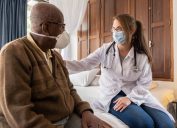 Doctor consoling senior patient at home - wearing face mask