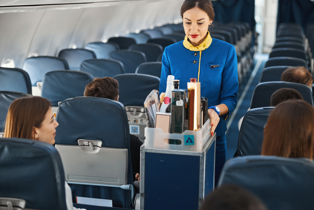 A flight attendant performing beverage service with drinks on a plane