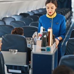 A flight attendant performing beverage service with drinks on a plane