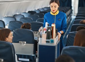 A flight attendant performing beverage service with drinks on a plane