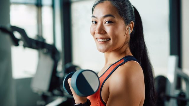 Happy asian athletic woman exercising with hand weights in a gym and picture id1361355221