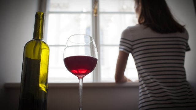 woman looking out the window with a glass of wine behind her