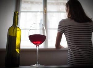woman looking out the window with a glass of wine behind her