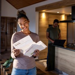 woman at home looking at a utility bill that came in the mail and smiling