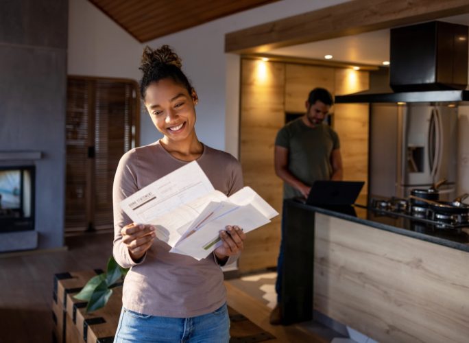 woman at home looking at a utility bill that came in the mail and smiling