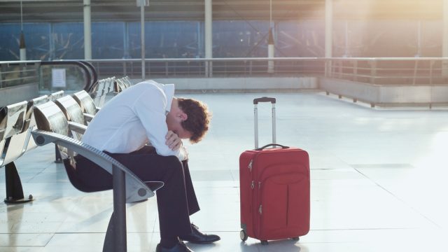 A man sitting near his suitcase in an airport after his flight was delayed or canceled