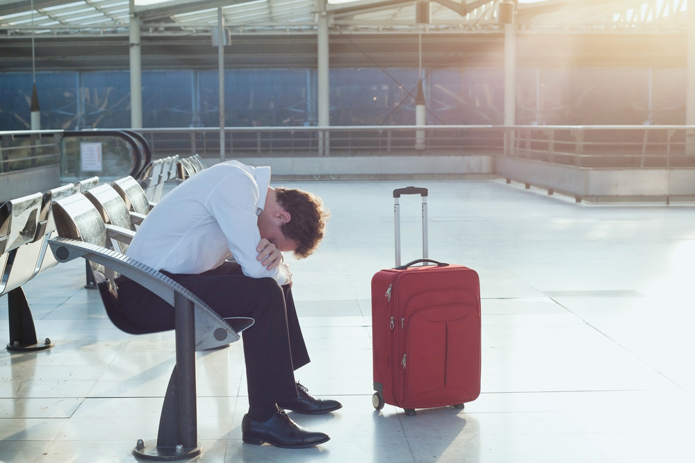 Ein Mann sitzt an einem Flughafen in der Nähe seiner Tasche, nachdem sein Flug verspätet oder annulliert wurde