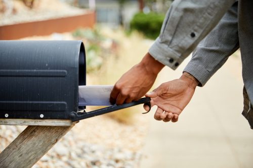 man standing outside of his house and taking an envelope out of his mailbox