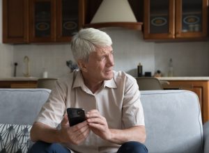 A senior man holding a smartphone with a concerned look on his face