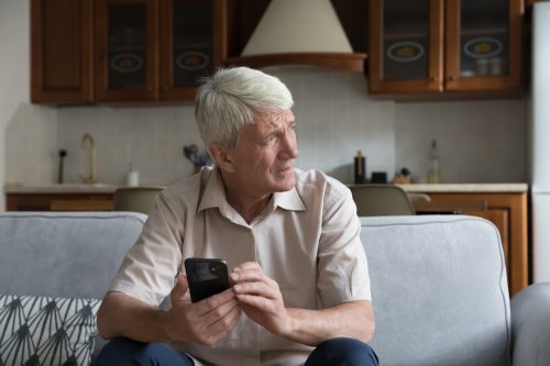 A senior man holding a smartphone with a concerned look on his face