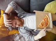 man lying on couch with remote control and pizza