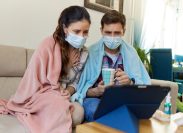 Scared couple in masks sitting on sofa and consulting online with a doctor over digital tablet