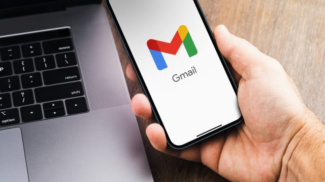 A close up of a hand holding a phone with the Gmail logo on it