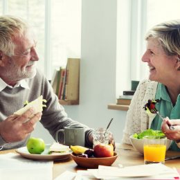 A senior couple eating breakfast together, including fruit, while smiling