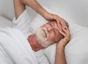 older man holding his head in bed