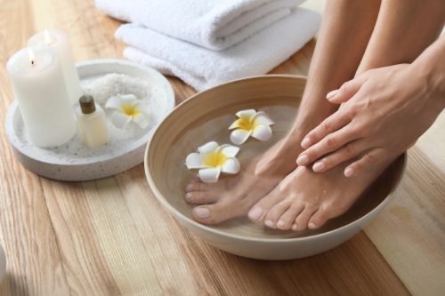 woman's feet soaking in a bowl with white flowers with towels next to it