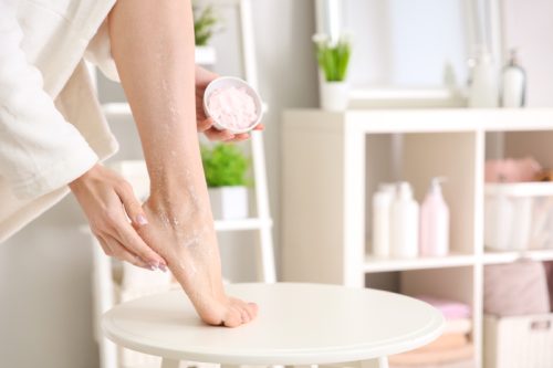 woman using an exfoliating rub on the heel of her foot in bathroom