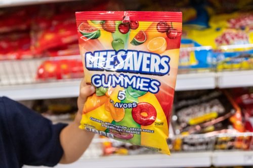 person holding a bag of life savers gummies in a candy aisle
