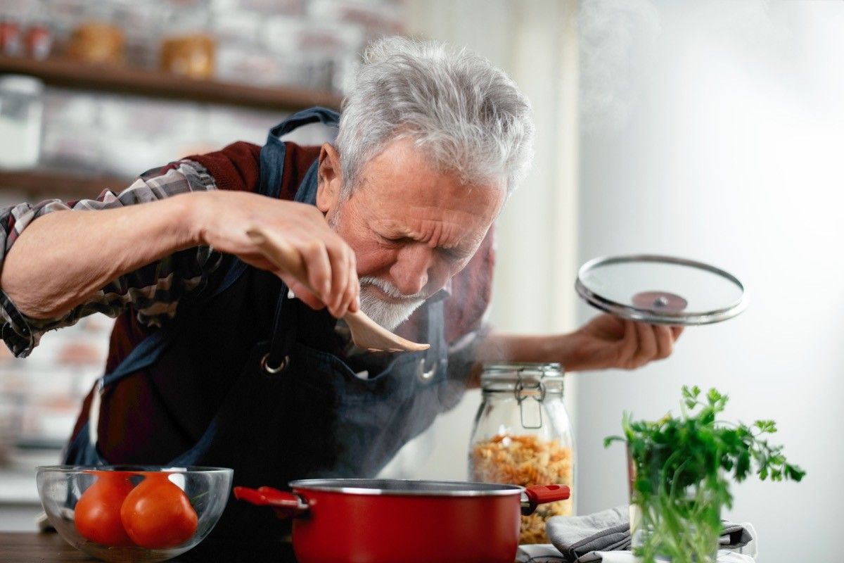 older man smelling sauce cooking