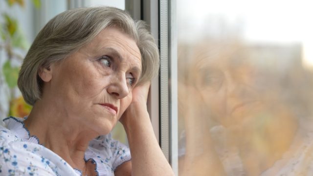 older woman looking out window holding head