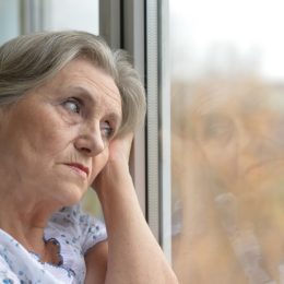 older woman looking out window holding head