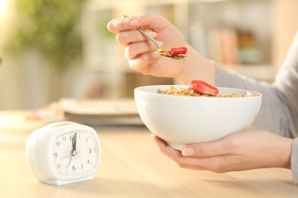 woman holding a bowl of cereal and watching a clock