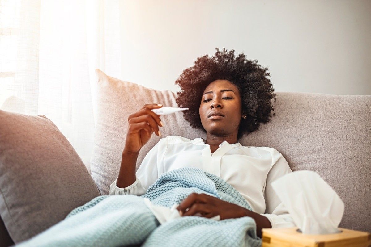 sick woman laying on couch checking temperature