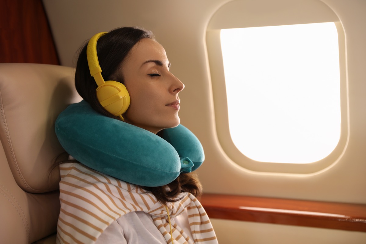 Woman Sleeping on a Plane using a teal neck pillow and yellow headphones
