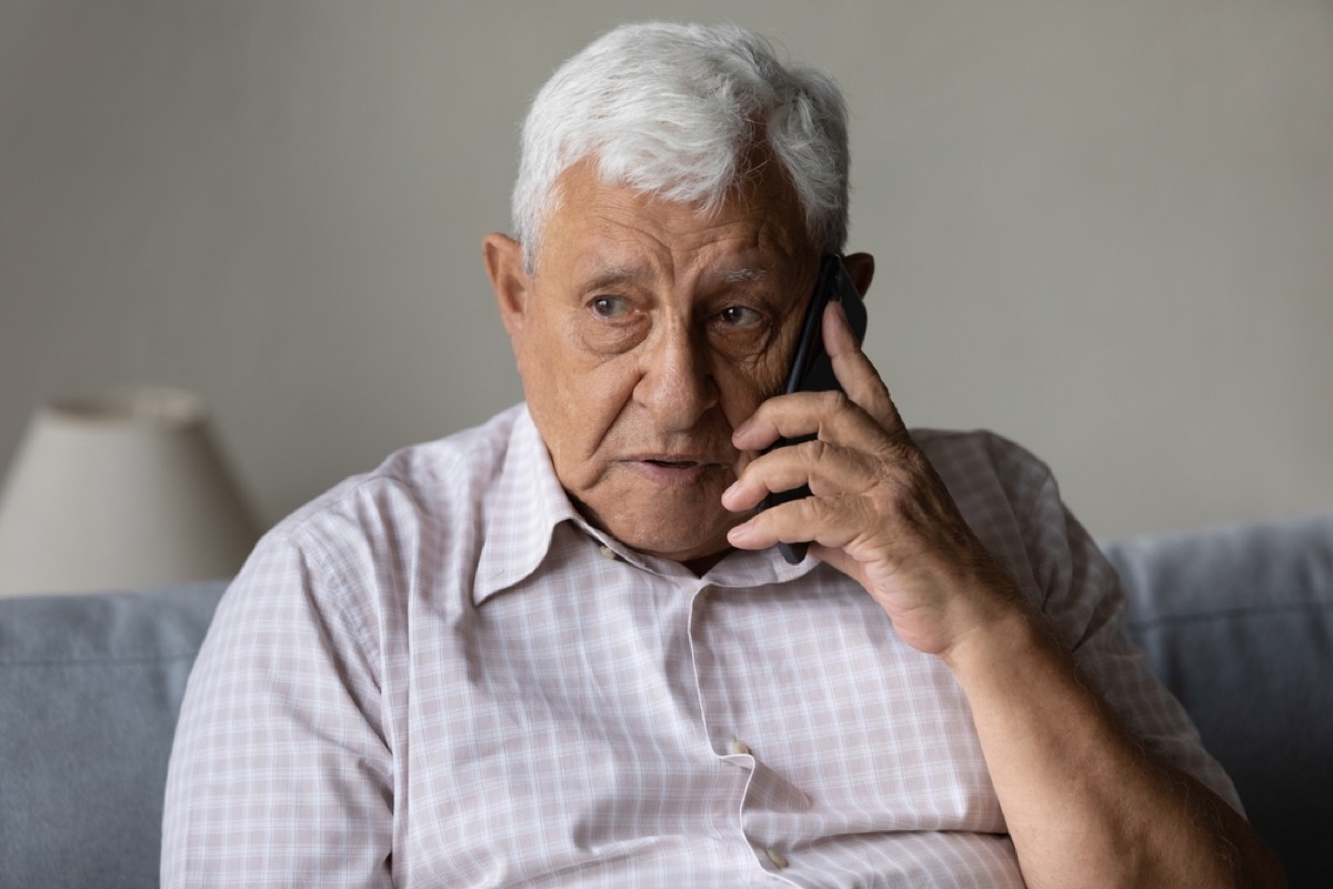 older man looking worried and concerned making a phone call on his couch