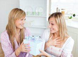 woman looking happy and surprised while friends gives her a big box with a bow on top