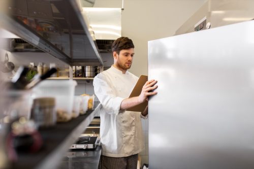 chef with checklist looking in restaurant fridge