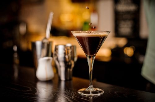 Espresso martini pe un bar cu boabe de espresso căzând în el