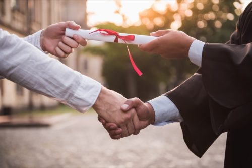 graduate in academic dress taking diploma and shaking hand