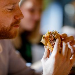 man holding a burger sandwich, sitting in a pub