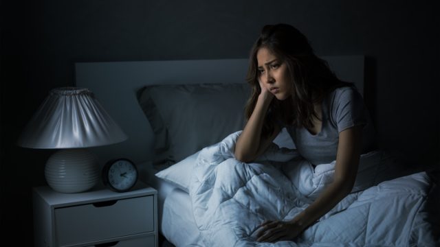 Woman sitting in bed cannot sleep from insomnia