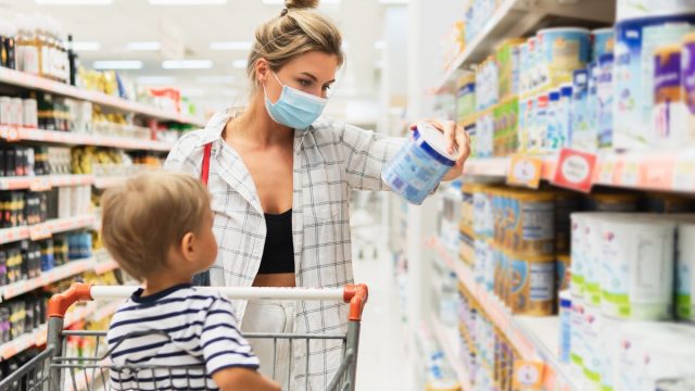 New normal in shopping. Young mother wearing prevention mask and her little son in a supermarket during virus pandemic.