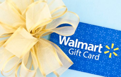 A horizontal studio shot of a WalMart gift card decorated with a gold bow, and shot on a blue background.
