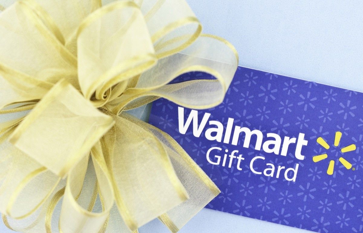 A horizontal studio shot of a WalMart gift card decorated with a gold bow, and shot on a blue background.