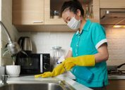 A woman cleaning her kitchen while wearing a face mask and gloves
