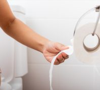 woman sitting on toilet tearing off toilet paper