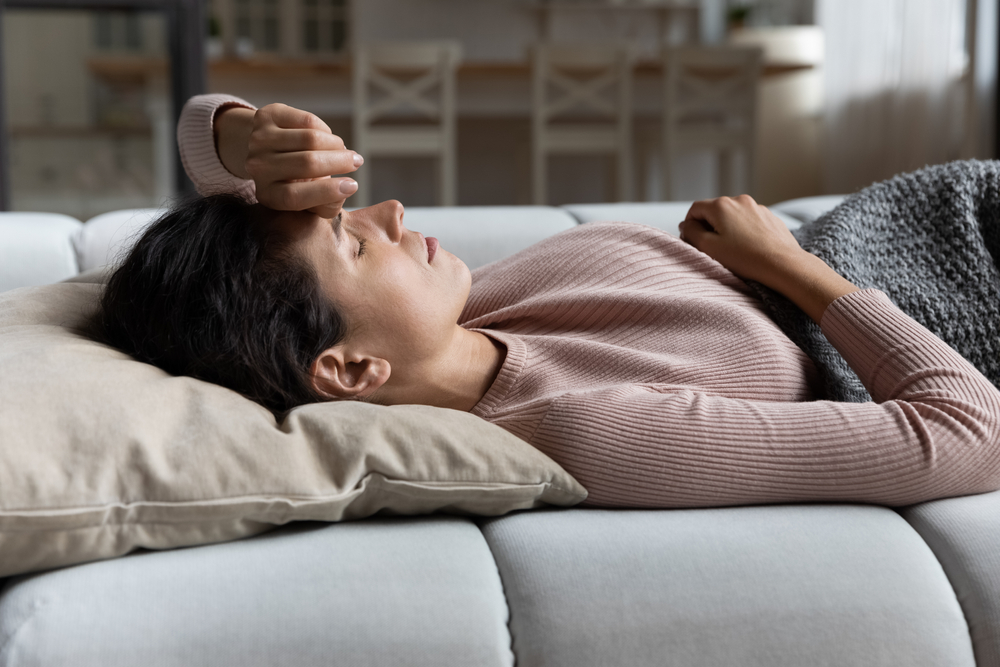 Junge Frau, die auf dem Sofa liegt und Symptome von Corona-Virus, Grippe oder Erkältung zeigt