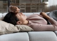 A young woman lying on the couch with symptoms of COVID, the flu, or a cold
