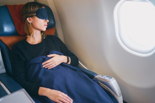 Frau, die in einem Flugzeug mit Decke und Augenmaske schläft