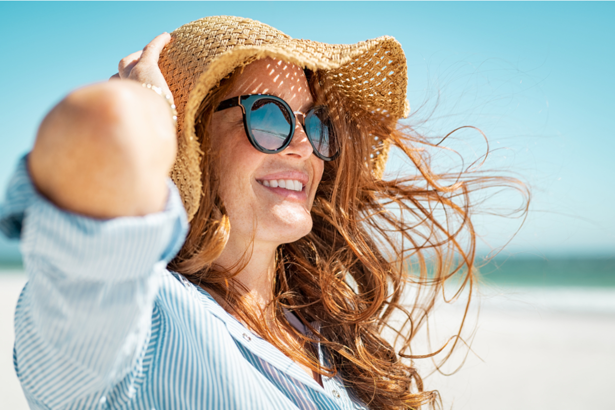 white woman on the beach wearing a sunhat and sunglasses